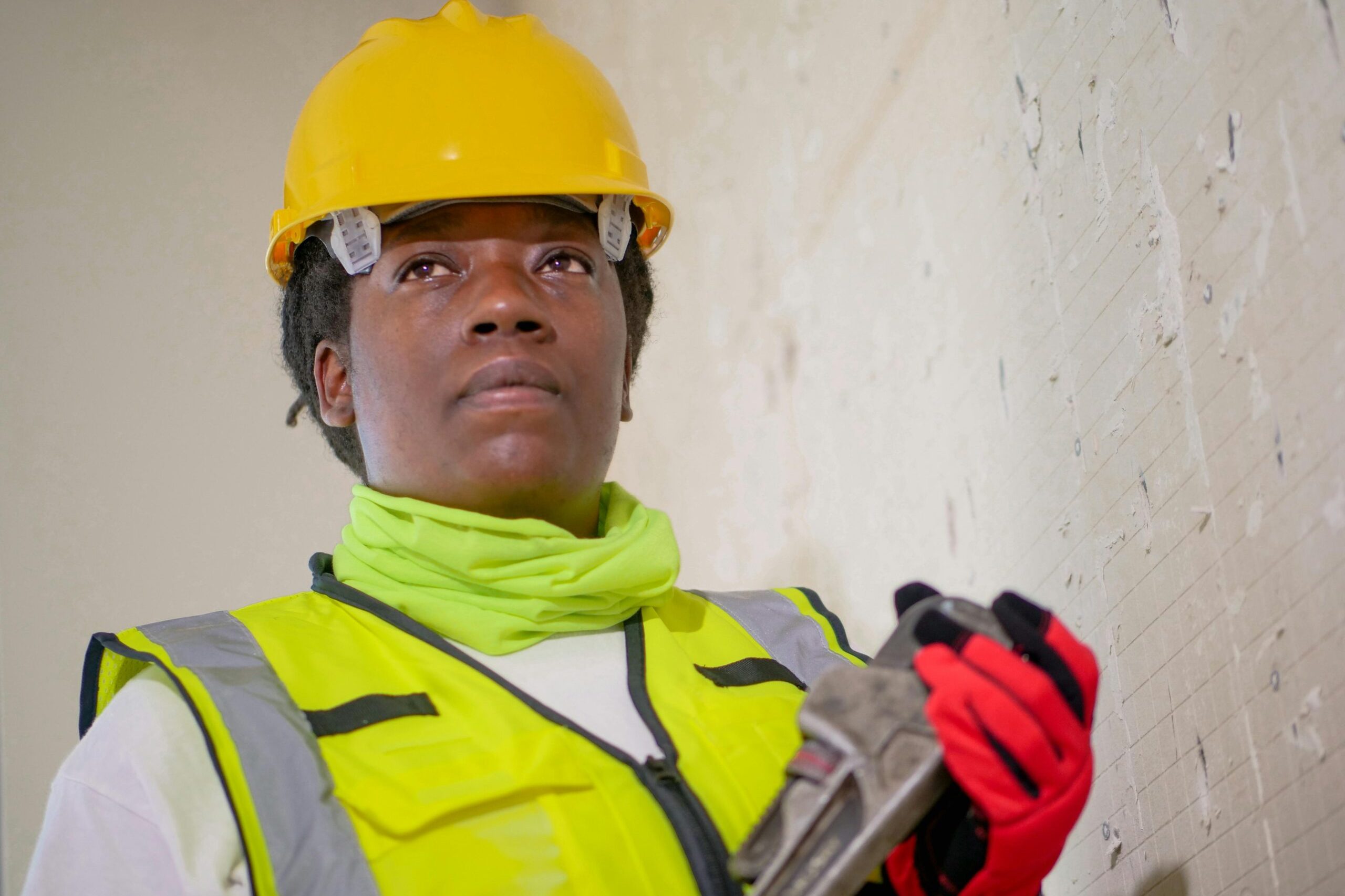 Portrait of a female construction worker in safety gear holding a wrench indoors.